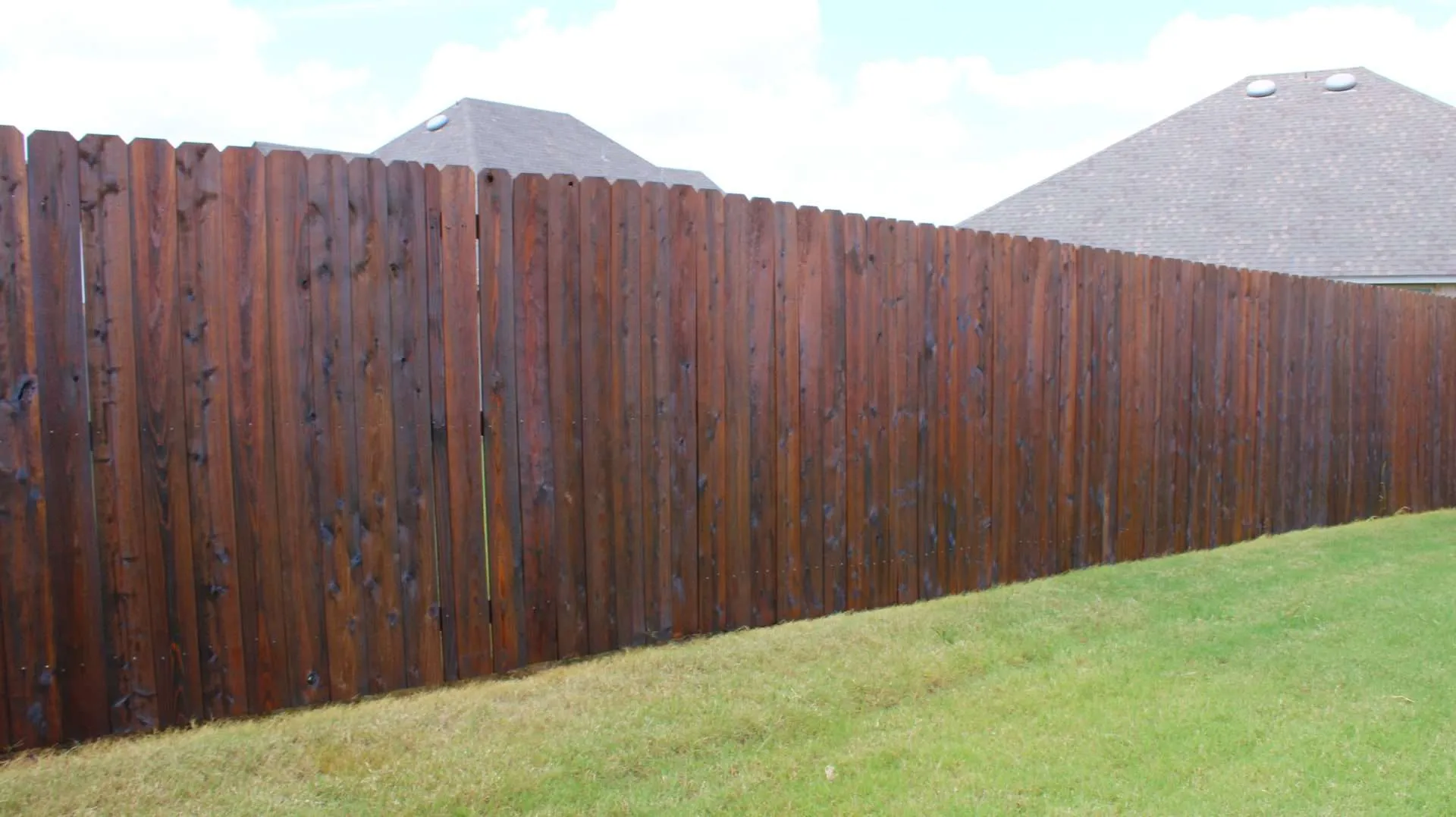 wood defender fence stain a long stretch of fence with dark brown fence stain on it.